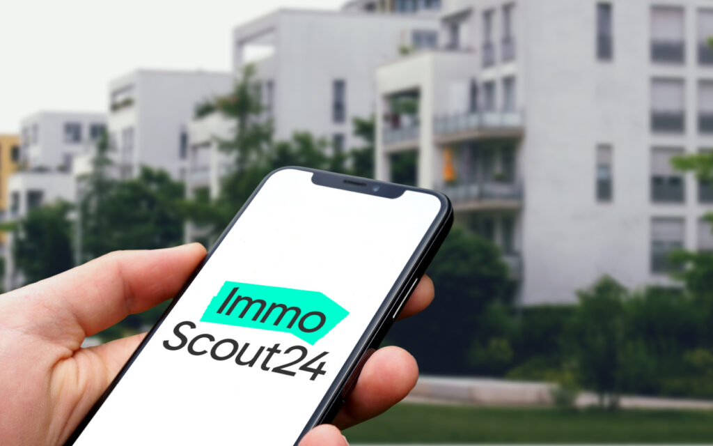Immoscout-Logo auf Smartphone, das jemand in der Hand hält