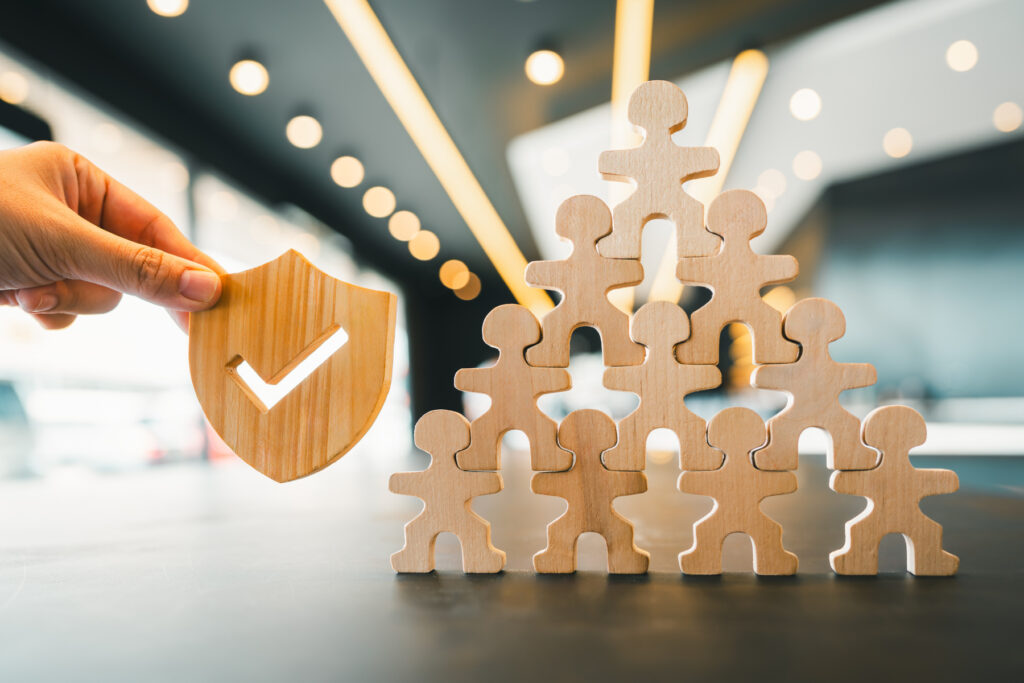 Wooden shield with check mark and team of wooden people figures symbolizing security, teamwork, protection, trust, corporate safety, and organizational support.